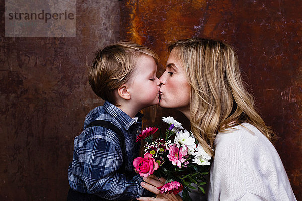 Junge gibt der Mutter einen Blumenstrauss  Mutter küsst den Jungen