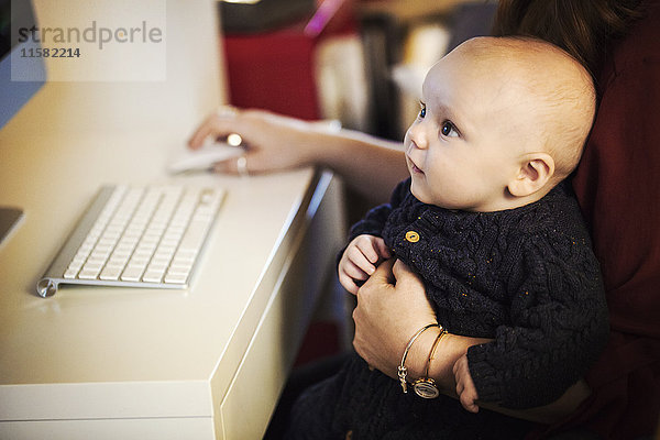 Ein Baby  das auf dem Knie eines Erwachsenen sitzt und auf einen Computerbildschirm schaut