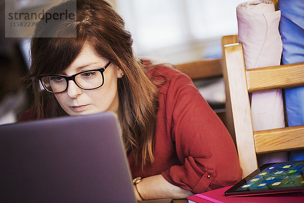 Eine junge Frau sitzt mit ihrem Laptop und lehnt sich an den Bildschirm  um den Inhalt zu lesen.