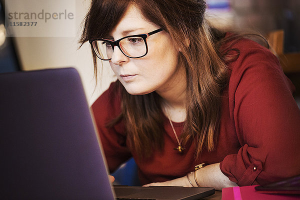 Eine junge Frau sitzt mit ihrem Laptop und lehnt sich an den Bildschirm  um den Inhalt zu lesen.