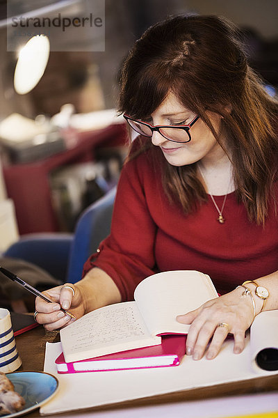 Eine Frau sitzt an einem Tisch  macht Notizen und schreibt in ein Notizbuch.