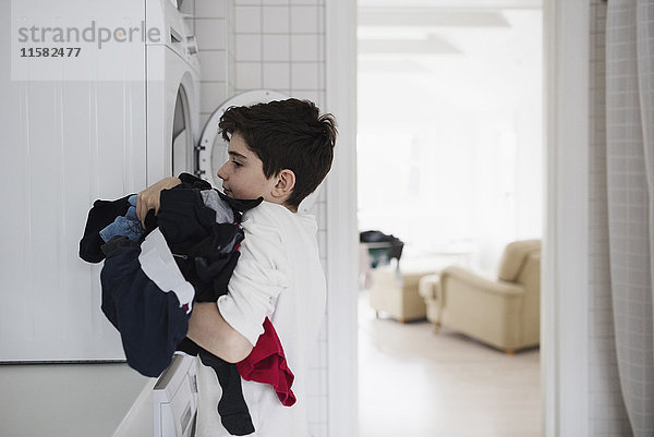 Seitenansicht des Jungen mit Wäsche in der Waschmaschine zu Hause