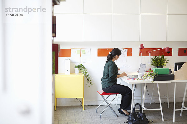 Durchgehende Seitenansicht der Geschäftsfrau mit Dokument und Laptop am Tisch im Büro