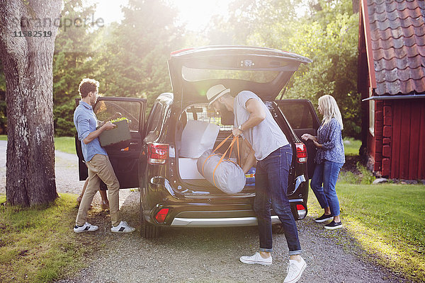 Volle Länge der Freunde beim Verladen des Gepäcks in das Auto an sonnigen Tagen.