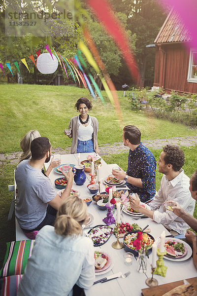 Fröhliche Frau im Gespräch mit Freunden bei Tisch in der Gartenparty