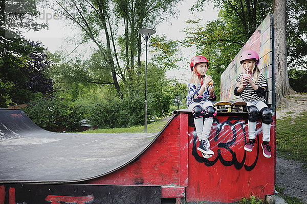 Freunde genießen Getränke  während sie auf der Skateboard-Rampe sitzen.