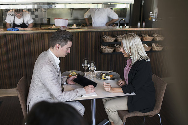 Geschäftsmann zeigt der Kollegin ein digitales Tablett  während sie im Restaurant am Tisch sitzt.