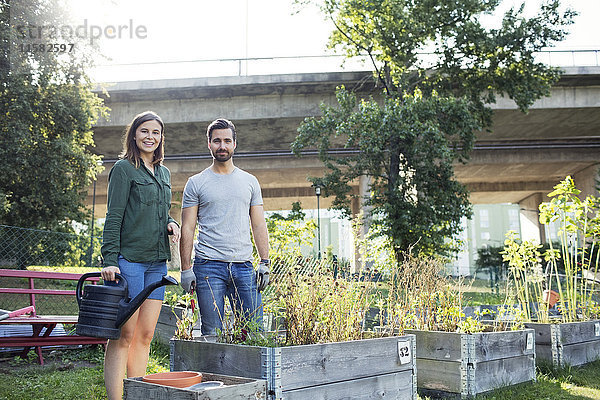 Porträt eines glücklichen mittleren Erwachsenenpaares mit Gießkanne im Stadtgarten