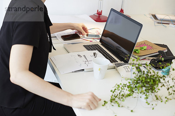 Mittelteil der Geschäftsfrau mit Handy mit Laptop und Dokument auf Tisch im Büro