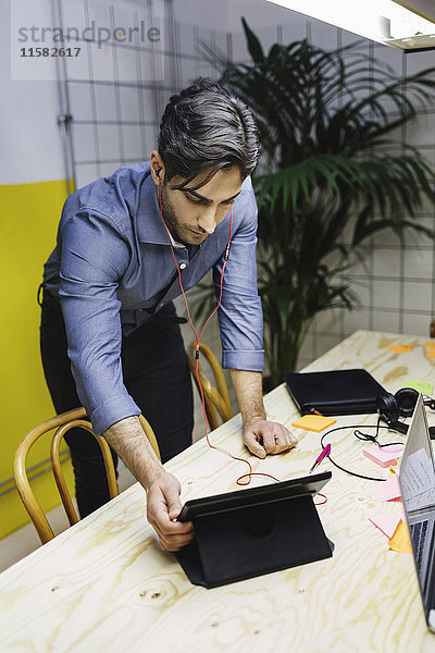 Junger Mann mit digitalem Tablett am Schreibtisch im Kreativbüro