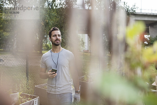 Mittlerer Erwachsener Mann mit Handy im Gemeinschaftsgarten