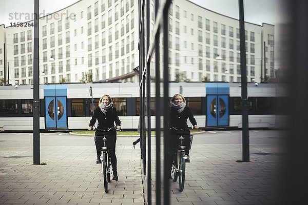 Volle Länge der mittleren erwachsenen Geschäftsfrau beim Fahrradfahren auf dem Bürgersteig in der Stadt