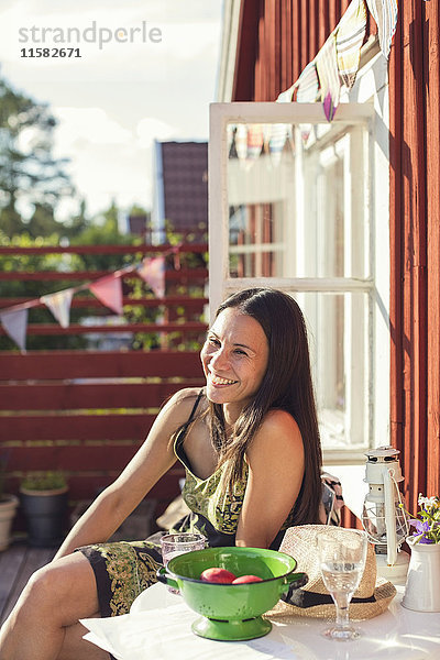 Fröhliche Frau am Tisch im Hinterhof an einem sonnigen Tag
