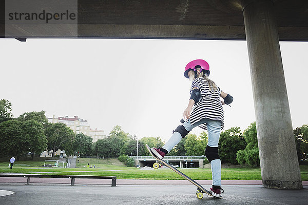 Volle Länge des Mädchens beim Stunt mit Skateboard im Park gegen den klaren Himmel