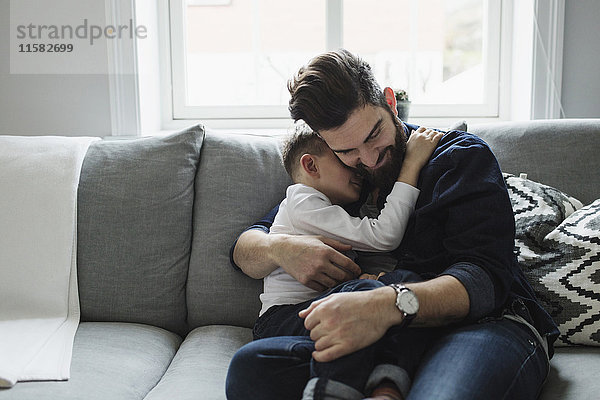 Vater umarmt den Sohn  während er zu Hause auf dem Sofa sitzt.