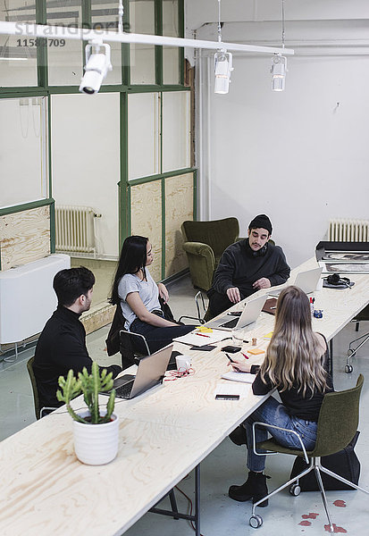Vier Unternehmer  die am Schreibtisch im kreativen Büro diskutieren