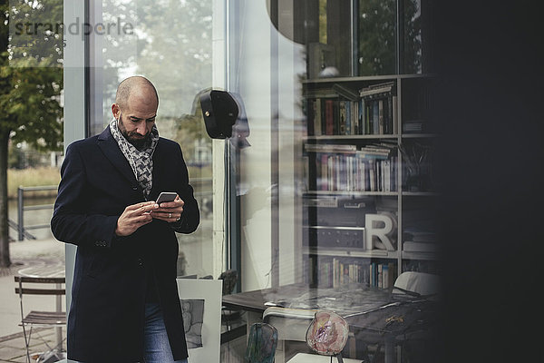 Mittlerer erwachsener Geschäftsmann  der ein Smartphone benutzt  während er durch den Laden läuft.