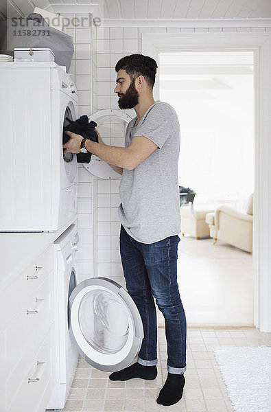 Seitenansicht des Mannes  der die Wäsche in der Waschmaschine zu Hause verlädt.