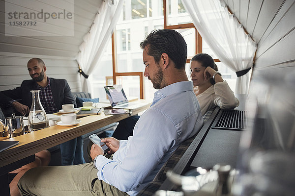 Mittlerer erwachsener Geschäftsmann mit Handy am Tisch während der Bürobesprechung