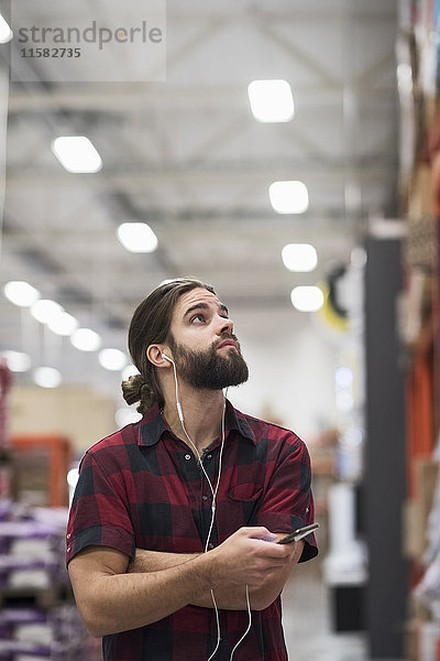 Männlicher Kunde schaut auf  während er Musik über ein Smartphone im Baumarkt hört.