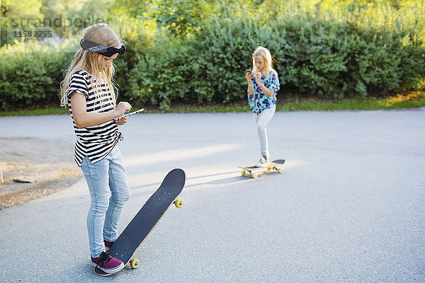 Freunde  die telefonieren  während sie mit Skateboards auf der Straße stehen.