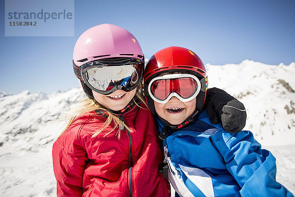 Fröhliche Geschwister in Skibekleidung gegen den schneebedeckten Berg stehend