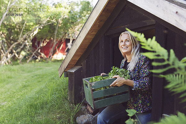 Lächelnde Frau mit Gemüsekiste beim Verlassen der Hütte