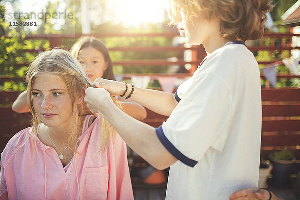 Freunde flechten die Haare von Teenagern im Garten.