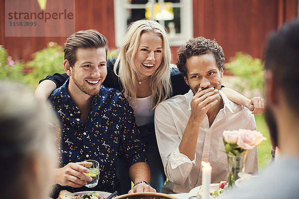Lächelnde Frau steht mit Freunden am Tisch in der Gartenparty