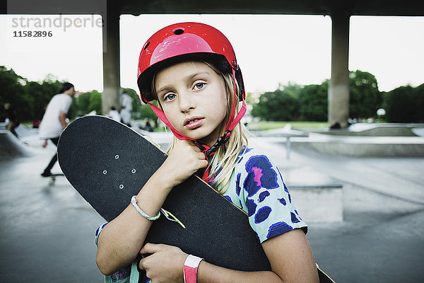 Porträt eines Mädchens mit rotem Helm und Skateboard im Park