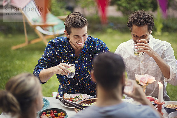 Glückliche Männer beim Trinken mit Freunden am Tisch in der Gartenparty