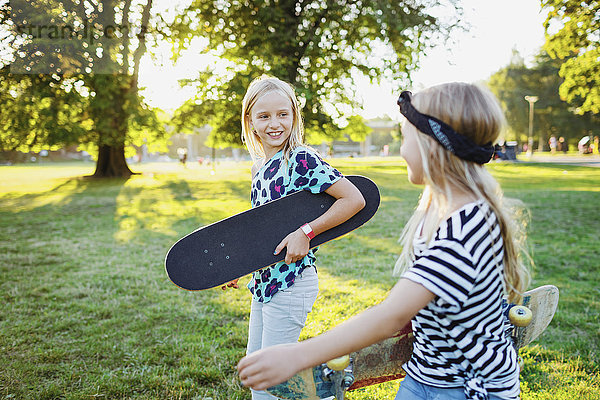 Lächelnde Freunde mit Skateboards  die auf dem Grasfeld spazieren gehen