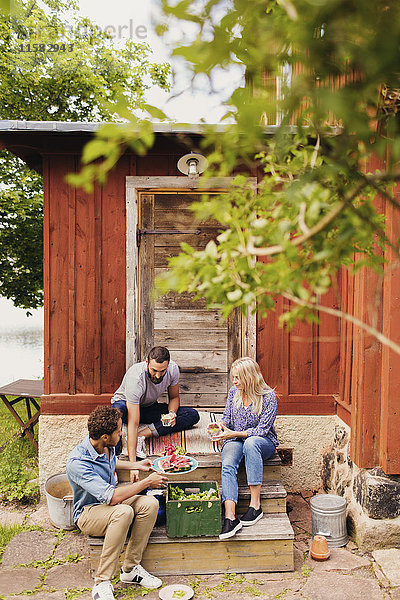 Freunde essen Wassermelone und trinken  während sie vor dem Haus sitzen.