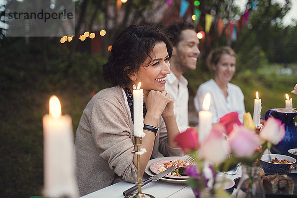 Lächelnde Freunde sitzen am geschmückten Tisch in der Gartenparty