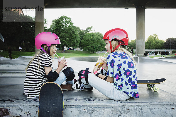 Freunde trinken Saft  während sie im Skateboard-Park sitzen.