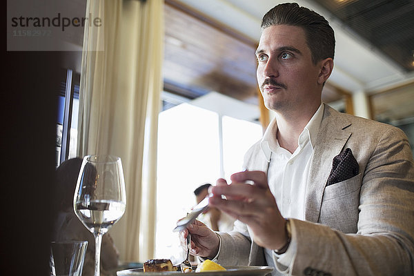 Geschäftsmann schaut weg  während er im Restaurant ein Smartphone hält.