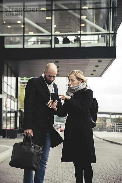 Geschäftsfrau zeigt Smartphone dem Geschäftsmann auf der Stadtstraße