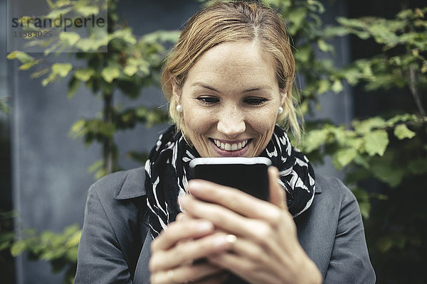 Lächelnde mittlere erwachsene Geschäftsfrau mit Smartphone im Freien