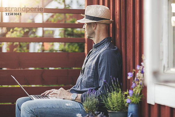 Seitenansicht des sitzenden Mannes mit Laptop im Hinterhof