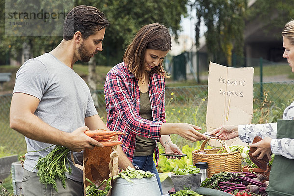 Mittleres erwachsenes Paar  das Gartengemüse an eine Kundin verkauft.