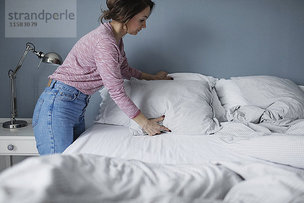 Seitenansicht der Frau  die die Kissen auf dem Bett zu Hause anordnet.
