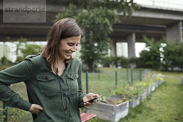 Lächelnde mittlere erwachsene Frau mit Handy im Gemeinschaftsgarten