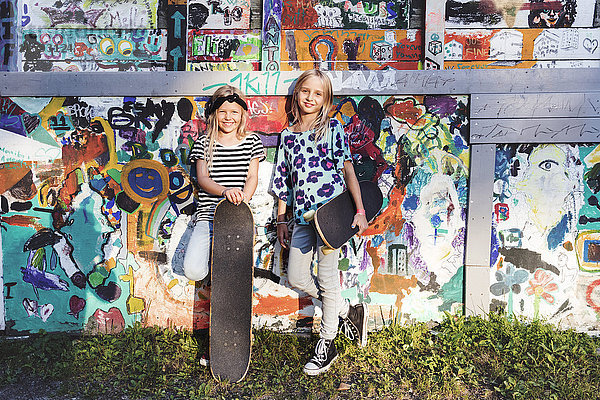 Volle Länge der Mädchen  die Skateboards halten  während sie an der Graffiti-Wand stehen.