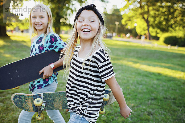 Portrait von glücklichen Freunden mit Skateboards beim Spaziergang auf der Wiese