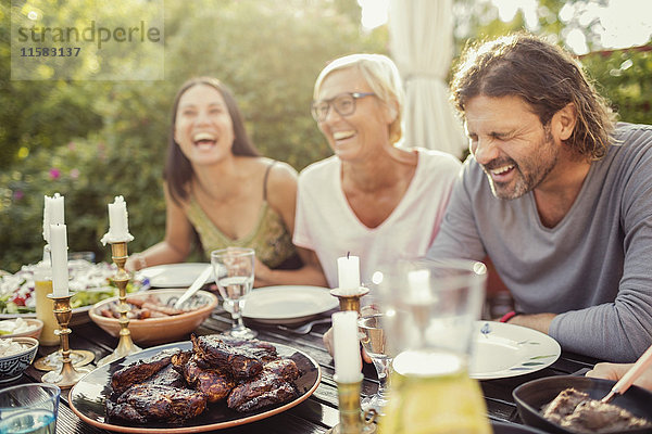 Fröhliches Paar und Freundin lachend auf dem Esstisch während der Gartenparty im Hinterhof