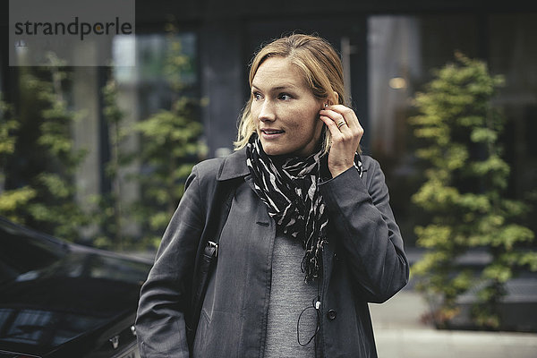 Mittlere erwachsene Geschäftsfrau mit Kopfhörern beim Überqueren der Straße