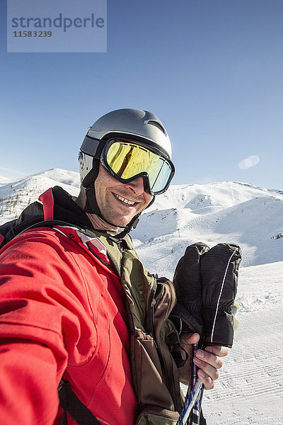 Lächelnder Mann in Skibekleidung steht auf schneebedecktem Feld gegen den klaren Himmel.