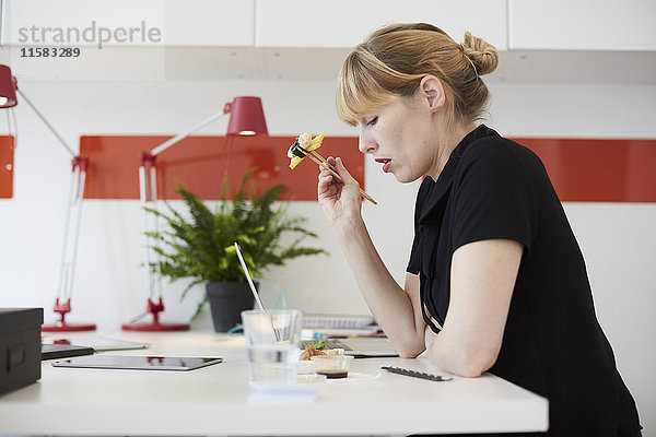 Seitenansicht der mittleren erwachsenen Geschäftsfrau beim Mittagessen am Tisch im Büro