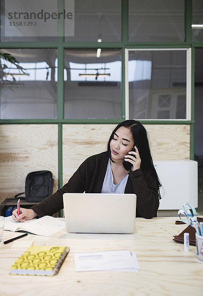 Frau mit Smartphone am Schreibtisch im Kreativbüro