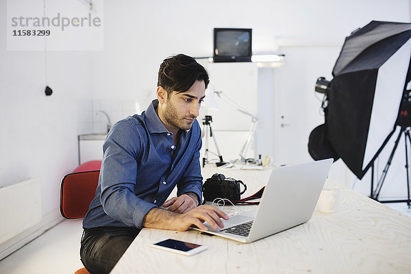 Männlicher Blogger mit Laptop am Schreibtisch im Kreativbüro